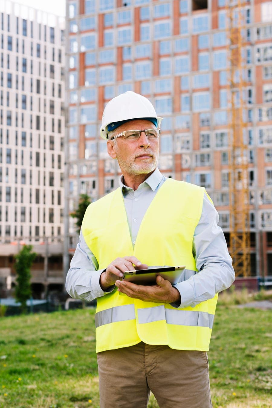 Ingeniero civil con casco y tableta frente a un edificio en construcción